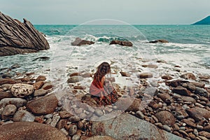 Beautiful young boho styled woman sitting on a stone beach photo