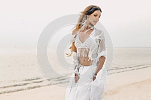 Beautiful young boho woman in white dress and feathers posing on