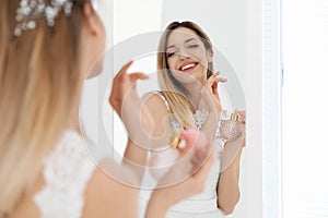 Beautiful young bride with bottle of perfume near mirror