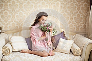 Beautiful young Bride with dark hairs sits on a sofa in a bedroom. Bride`s morning.