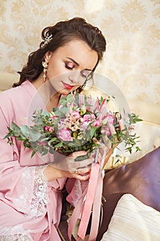 Beautiful young Bride with dark hairs sits on a sofa in a bedroom. Bride`s morning.