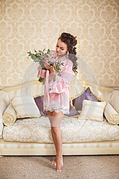 Beautiful young Bride with dark hairs sits on a sofa in a bedroom. Bride`s morning.