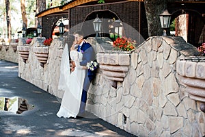 Beautiful young bride and groom kissing near the stone wall in the park. Wedding couple in love at wedd day