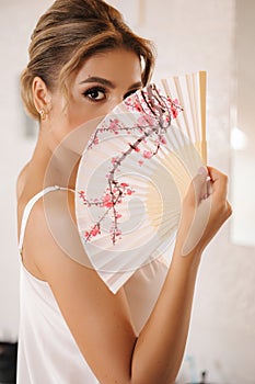Beautiful young bride holds a traditional Japanese fan in her hands and covers half of her face with it
