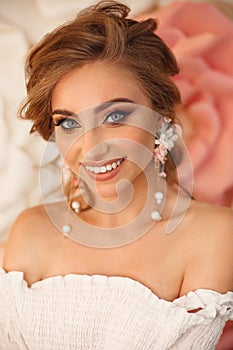 Beautiful young bride with makeup and fashion wedding hairstyle. Closeup portrait of young gorgeous woman over roses flowers.