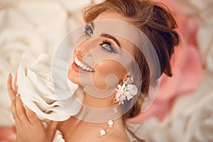 Beautiful young bride with makeup and fashion wedding hairstyle. Closeup portrait of young gorgeous woman over roses flowers.