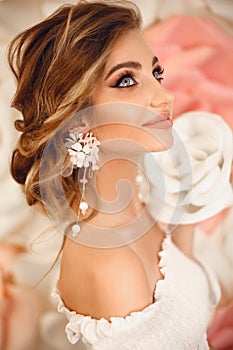 Beautiful young bride with makeup and fashion wedding hairstyle. Closeup portrait of young gorgeous woman over roses flowers.