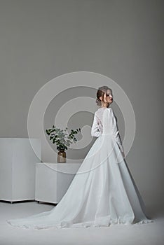 A beautiful young bride model in long lace dress in minimalist white studio interior. Wedding photography