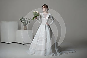 A beautiful young bride model in long lace dress in minimalist white studio interior. Wedding photography