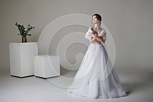 A beautiful young bride model in long lace dress in minimalist white studio interior. Wedding photography