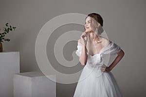 A beautiful young bride model in long lace dress in minimalist white studio interior. Wedding photography