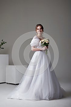 A beautiful young bride model in long lace dress in minimalist white studio interior. Wedding photography