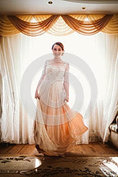 Beautiful young bride near the window in full growth