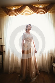 Beautiful young bride near the window in full growth