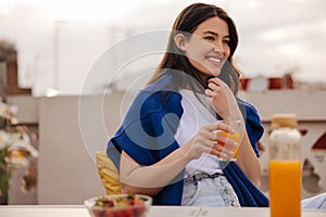 Beautiful young brunette caucasian woman is drinking orange cocktail in summer on terrace.