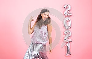 Young woman on a pink background with silver ballons in the form of the numbers 2021 photo