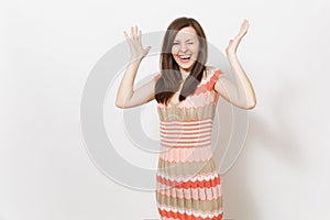 Beautiful young brunette girl in light beige and pink patterned dress rejoices, croaks funny faces and spread hands in