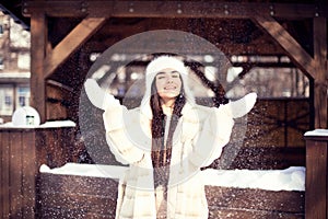 Beautiful young brunette girl with long hair in a white fur coat and a white hat has fun at the resort.