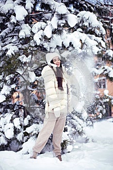 Beautiful young brunette girl with long hair in a white fur coat and a white hat has fun at the resort.