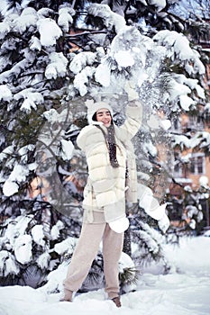 Beautiful young brunette girl with long hair in a white fur coat and a white hat has fun at the resort.