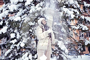 Beautiful young brunette girl with long hair in a white fur coat and a white hat has fun at the resort.