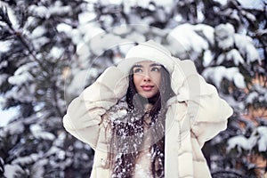 Beautiful young brunette girl with long hair in a white fur coat and a white hat has fun at the resort.