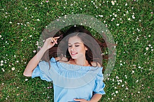 Beautiful young brunette girl looking away and lying on a clearing among white flowers