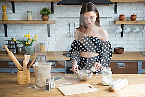A beautiful young brunette girl in a polka-dot dress kneads a dough and drives in eggs for a cake. Woman cooks in the kitchen