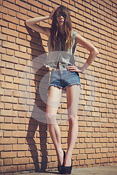 Beautiful young brunette in jeans clothes posing outdoor near red brick wall