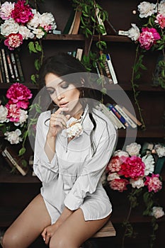 Beautiful and young brunette model woman with big lips and closed eyes, only in shirt posing half-naked in library