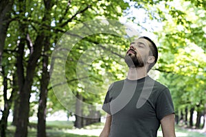 A beautiful young brunette is standing in the park, raising his head to the top and closing his eyes and enjoying life