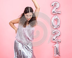 Young woman on a pink background with silver ballons in the form of the numbers 2021 photo