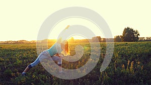 Beautiful young brunette woman doing yoga exercise on the field during amazing sunset.