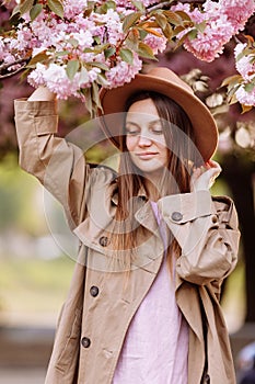 Beautiful young brunette woman with long hair flying in the wind and brown hat in a flowering garden. shallow depth of field.