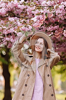 Beautiful young brunette woman with long hair flying in the wind and brown hat in a flowering garden. shallow depth of field.