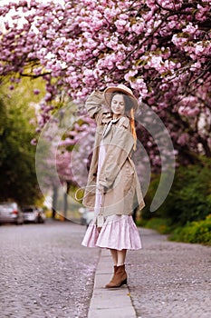 Beautiful young brunette woman with long hair flying in the wind and brown hat in a flowering garden. shallow depth of field.