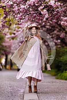 Beautiful young brunette woman with long hair flying in the wind and brown hat in a flowering garden. shallow depth of field.