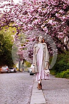 Beautiful young brunette woman with long hair flying in the wind and brown hat in a flowering garden. shallow depth of field.