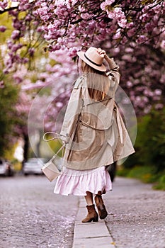 Beautiful young brunette woman with long hair flying in the wind and brown hat in a flowering garden. shallow depth of field.