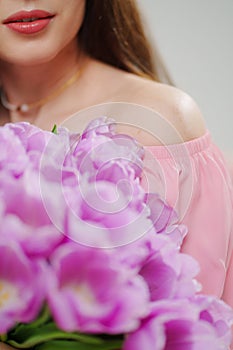 beautiful young brunette woman with long hair in pink with a bouquet of tulips.