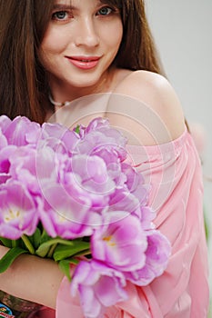 beautiful young brunette woman with long hair in pink with a bouquet of tulips.