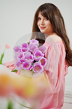 beautiful young brunette woman with long hair in pink with a bouquet of tulips.