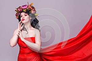 Beautiful young brunette woman model with bright flowers on her head in long red dress  on the purple background