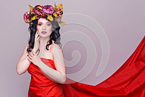 Beautiful young brunette woman model with bright flowers on her head in long red dress  on the purple background