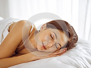 Beautiful young brunette woman sleeping while lying in bed comfortably and blissfully. Good morning concept