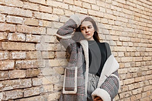 Beautiful young brunette woman in vintage gray pants in a black shirt in a fashionable plaid jacket posing standing