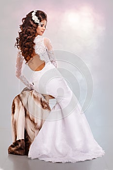 Beautiful young brunette woman in a wedding dress sits on a mink coat back