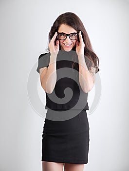 Beautiful young business smiling woman standing in black office formal clothing and holding hands the eye glasses on blue