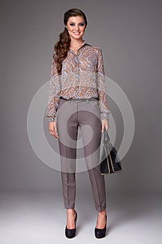 Beautiful young business woman with evening make-up dressed in tight pants and silk blouse with lace long sleeves and high-he