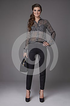 Beautiful young business woman with evening make-up dressed in tight pants and silk blouse with lace long sleeves and high-he